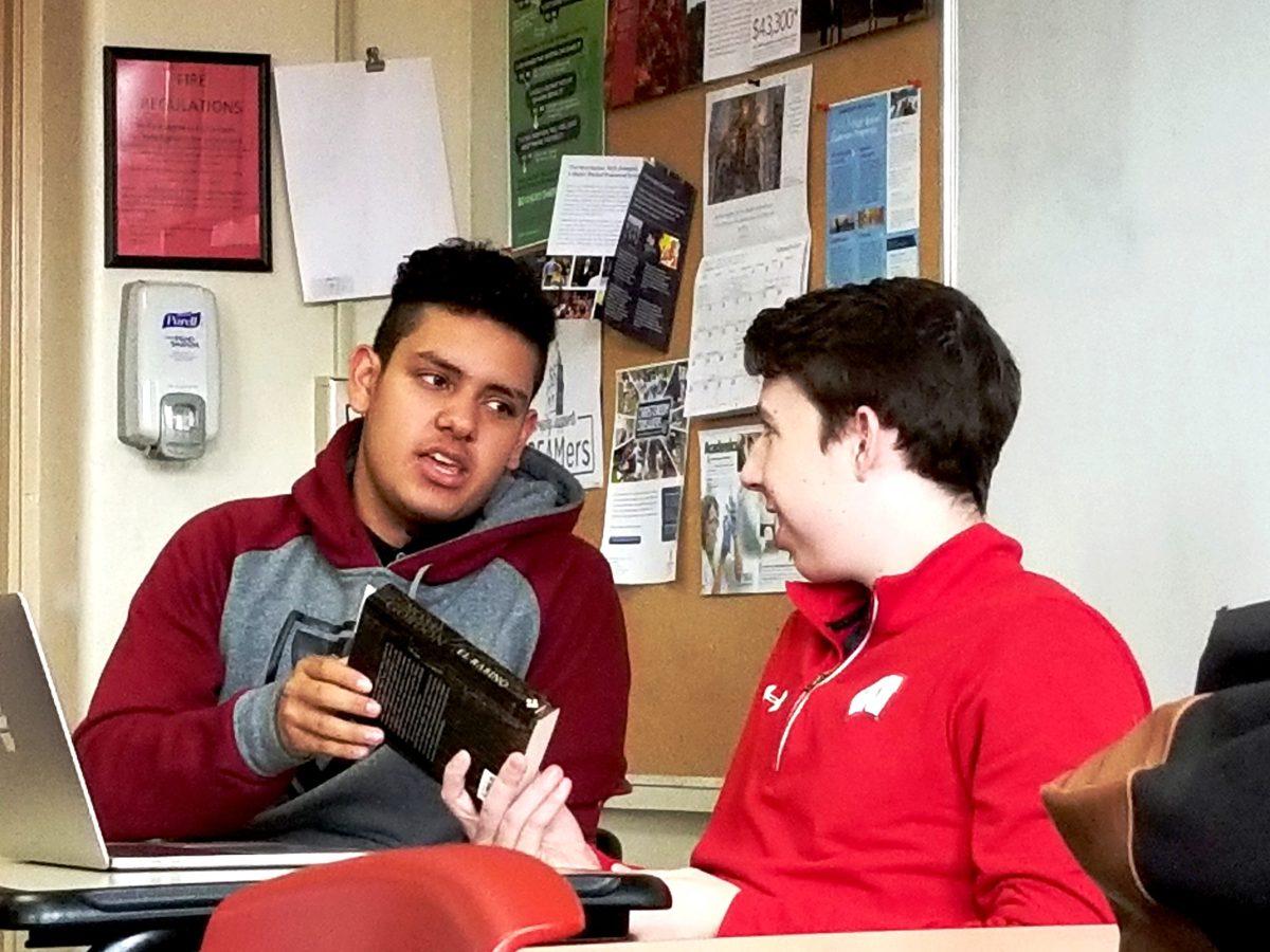 Photo by Manuel Mata-Flores ’19 | Ryan Schmit’19 talks to his preuvian student, insert name here, over a book in his ethics class during period one on Friday Feb. 16, 2018.