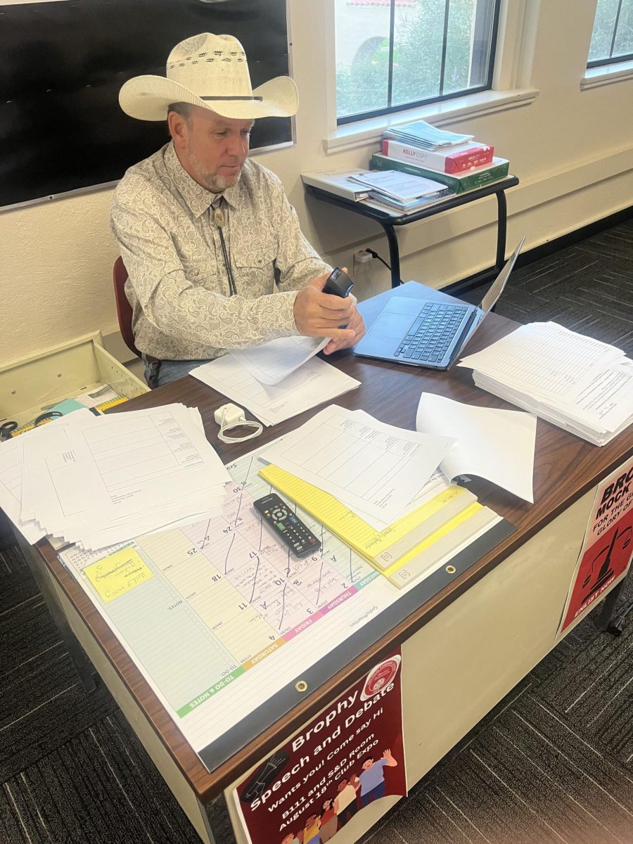 Mr. Paul Hamel (dressed up for halloween) staples papers for  Freshman World Seminar and AP US History.
